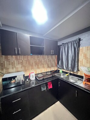Une cuisine avec des meubles de couleur noire, une cuisinière à gaz, une bouilloire et un évier.