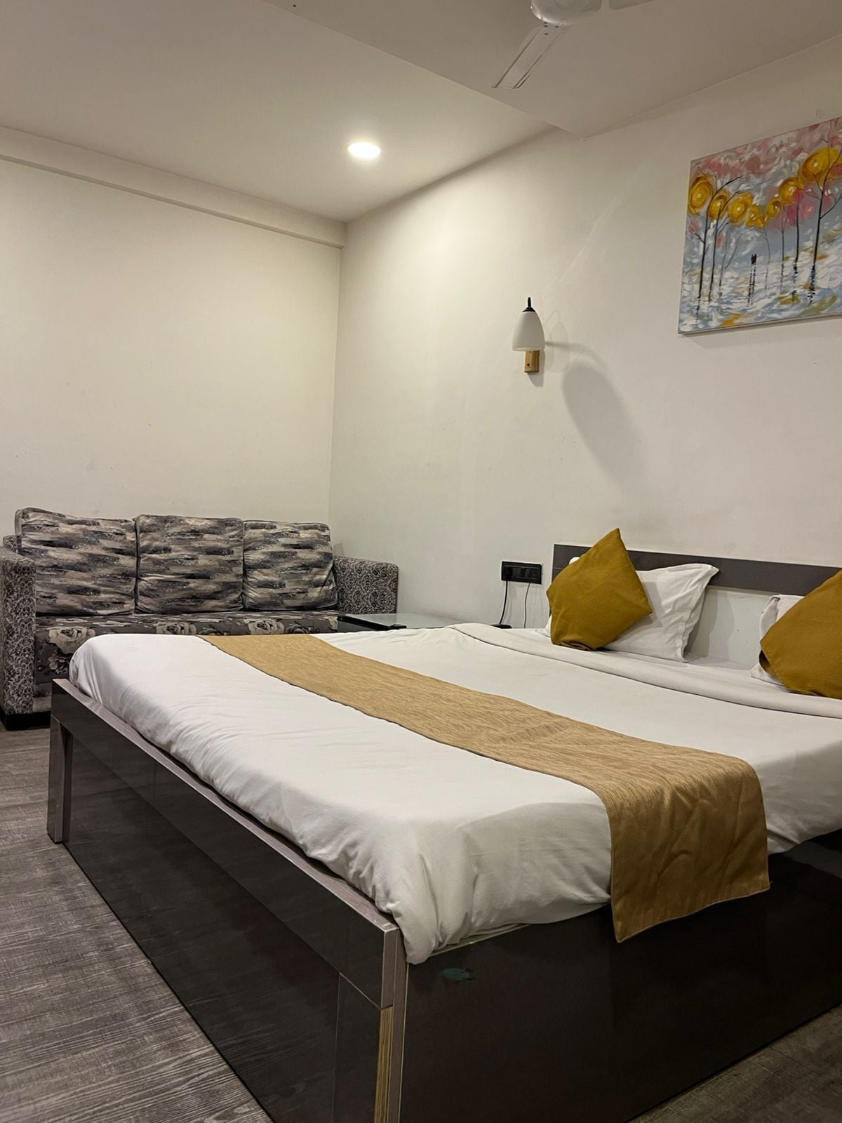 Quarto de hotel com cama, sofá, quadro e luminária na parede.