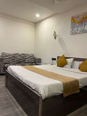 A hotel room with a bed, a sofa, a painting, and a wall-mounted lamp. - The Boss (Hingna)