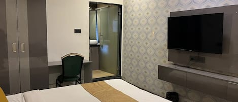 Quarto de hotel com cama, uma cadeira, televisão e guarda-roupa.