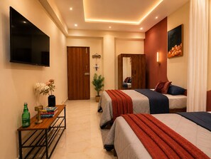 A hotel room with two beds, a flat-screen TV, a wooden wardrobe, a bedside table with books and a bottle, and a potted plant. - C Suites Shelton (Bengaluru)