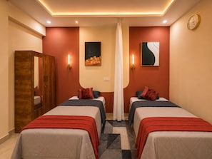 A hotel room with two beds, a wardrobe, wall-mounted artwork, and a clock. - C Suites Shelton (Bengaluru)