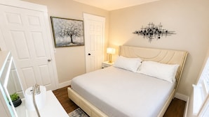 Un dormitorio con cama, mesita de noche, lámpara y una obra de arte en la pared.