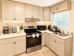 A kitchen with light-colored cabinets, a stainless steel oven, a microwave, and a window with blinds.