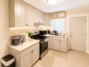 A kitchen with white cabinets, a black oven, a coffee maker, and a window with blinds.