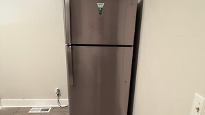 Un refrigerador de acero inoxidable en una cocina con piso de baldosas y pared blanca.