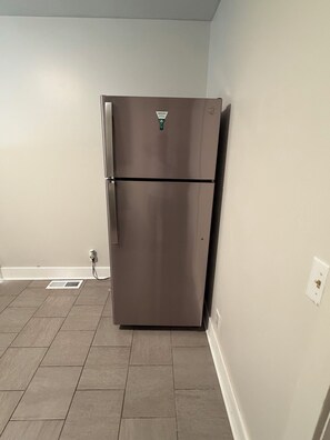 A stainless steel refrigerator in a kitchen with tiled flooring and a white wall.