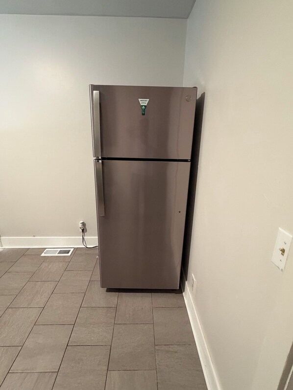 A stainless steel refrigerator in a kitchen with tiled flooring and a white wall.