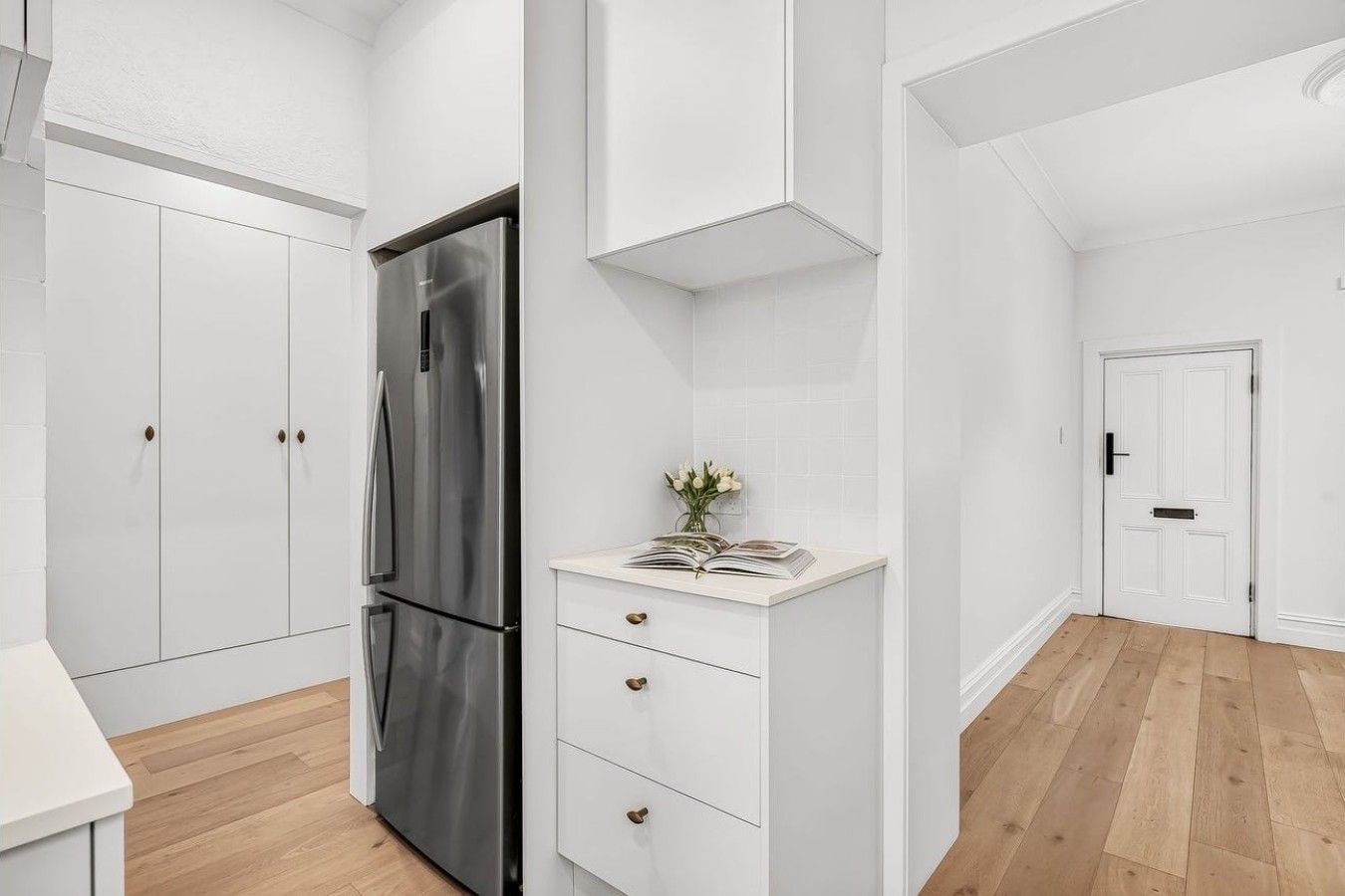 A modern kitchen with white cabinetry, a stainless steel refrigerator, and a wooden floor.