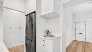 A modern kitchen with white cabinetry, a stainless steel refrigerator, and a wooden floor. - Renovated character cottage, walk to Melbourne St and the city (North Adelaide)