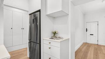 A modern kitchen with white cabinetry, a stainless steel refrigerator, and a wooden floor.