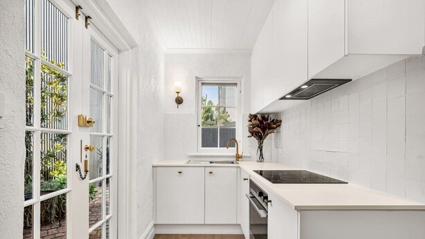 A compact kitchen with white cabinetry, a window, and a view of greenery outside. - Renovated character cottage, walk to Melbourne St and the city (North Adelaide)
