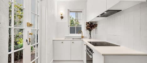 Cocina pequeña con armarios blancos, una ventana y vista a zonas verdes.