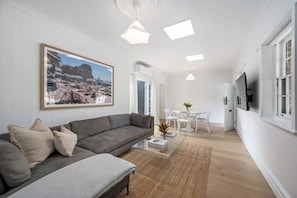 Ein modernes Wohnzimmer mit einem grauen Sofa, einem Couchtisch und einem Gemälde, das eine Strandansicht zeigt.