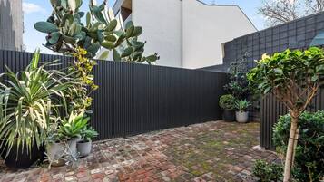 A courtyard with a brick floor, potted plants, and a black fence.