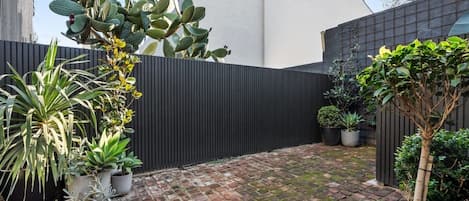 Une cour avec un sol en briques, des plantes en pot et une clôture noire.