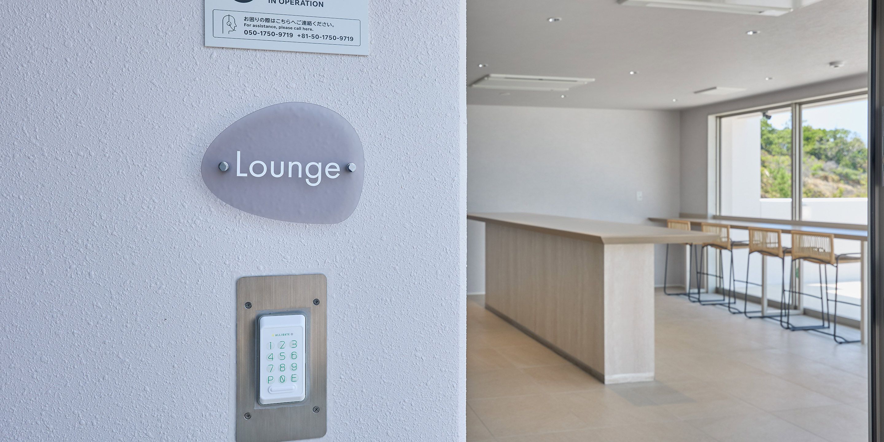 A lounge area with a sign indicating its location, a keypad for room access, and a view of the interior with a counter and seating area.