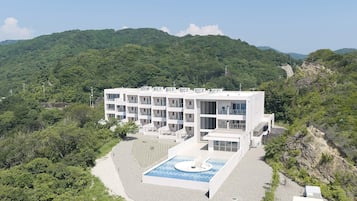 A multi-story hotel with a pool and a view of a forested mountain.