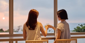 Deux personnes sont assises près d’une fenêtre, d’où elles peuvent admirer le coucher du soleil.