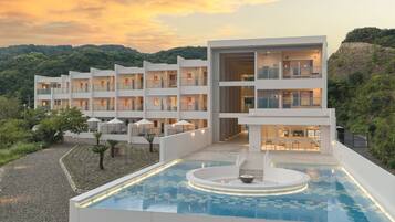 A modern hotel with multiple balconies, a swimming pool, and a view of the surrounding hills.