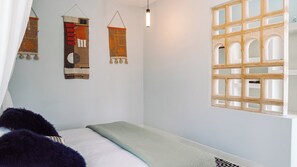 A bedroom with a bed, a window with a wooden lattice design, and two wall hangings. - Peaceful 4-bedroom villa in Watamu Kenya. (Watamu)