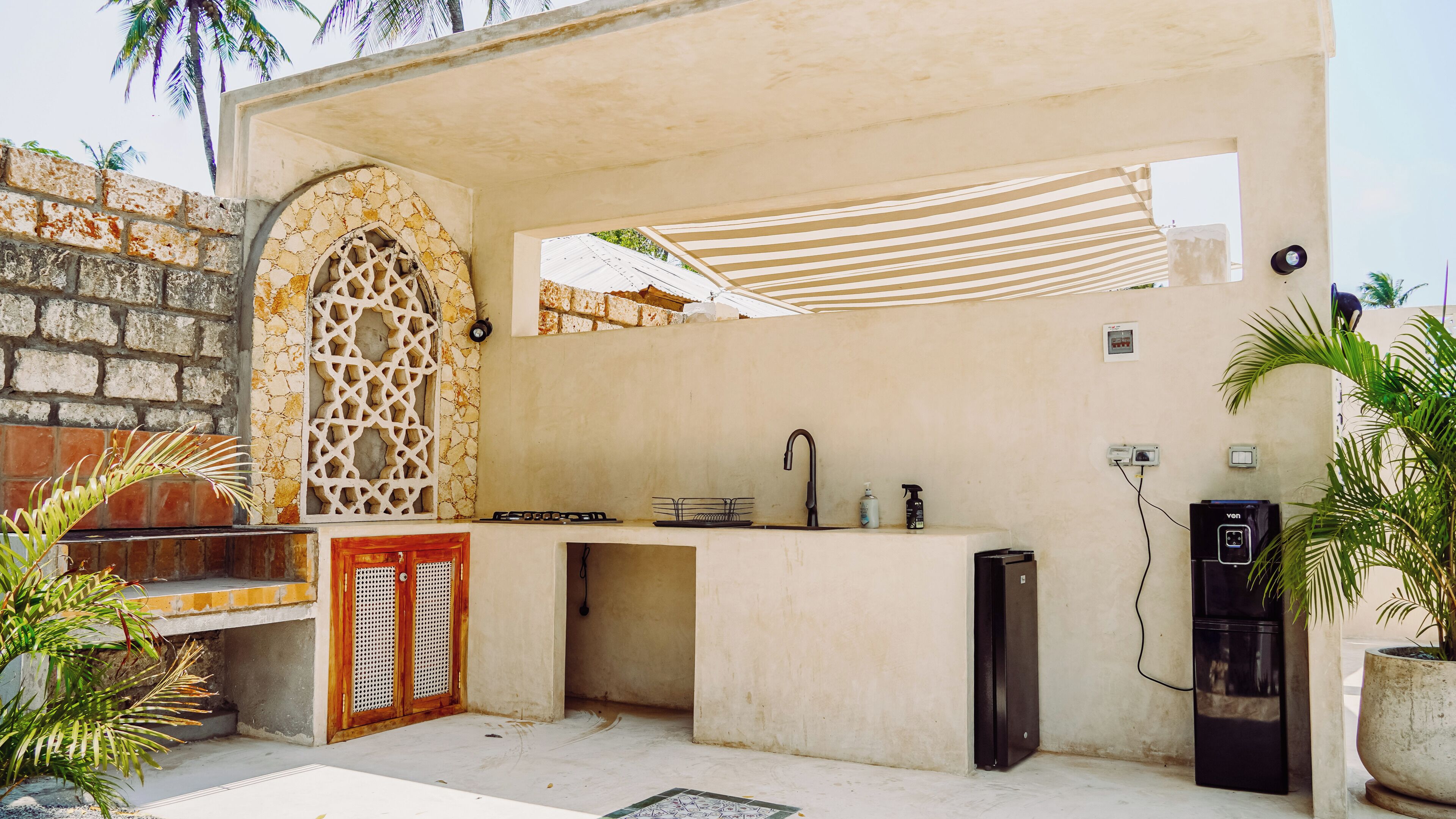 An outdoor kitchen area with a stone archway, a sink, a power outlet, and a small refrigerator.