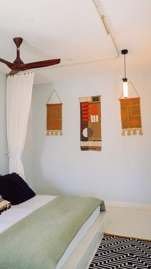 Ein Schlafzimmer mit einem Bett, einem Deckenventilator, einer Hängeleuchte und drei Wandteppichen.