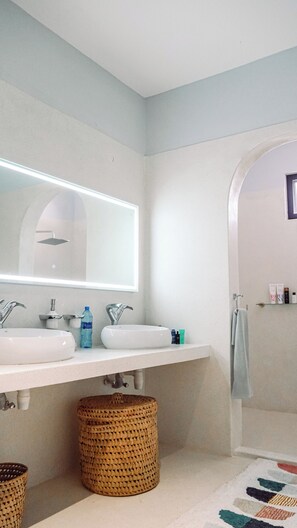 A bathroom with two sinks, a mirror, and a shower. There are toiletries on the counter and a towel hanging on the wall. - Peaceful 4-bedroom villa in Watamu Kenya. (Watamu)