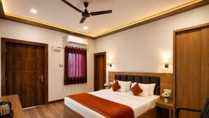 A hotel room with a bed, a desk, a chair, a small table with a plant, and a ceiling fan. - Swatik Resort By Amaratva (Vrindavan)