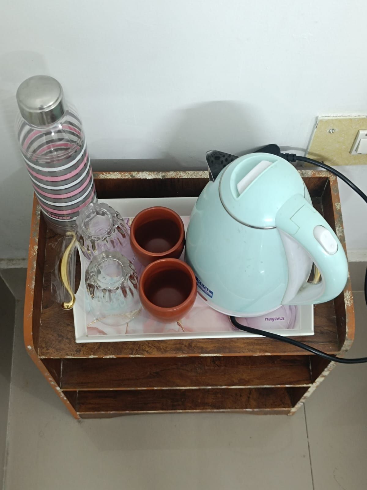 Una bandeja de madera con un hervidor verde azulado, dos tazas de terracota, un recipiente de vidrio y una botella a rayas.
