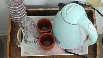 Una bandeja de madera con un hervidor verde azulado, dos tazas de terracota, un recipiente de vidrio y una botella a rayas.