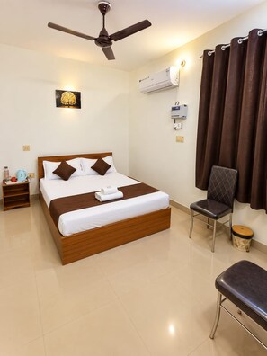A hotel room with a bed, a chair, a bedside table, an air conditioning unit, and a ceiling fan. - Raghav Guest House (Lalpur)