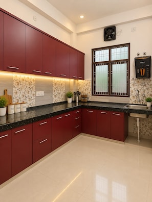 A modern kitchen with red cabinets, a black countertop, and a window with a view. - Raghav Guest House (Lalpur)