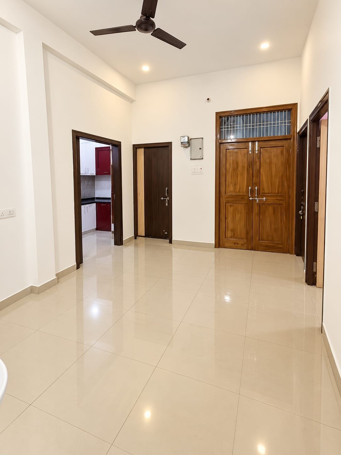 A spacious room with a ceiling fan, a large wooden door, and a tiled floor.