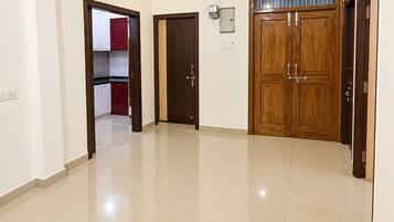 A spacious room with a ceiling fan, a large wooden door, and a tiled floor.