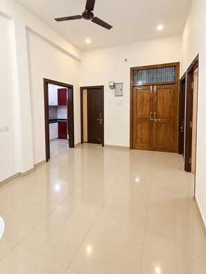 A spacious room with a ceiling fan, a large wooden door, and a tiled floor. - Raghav Guest House (Lalpur)