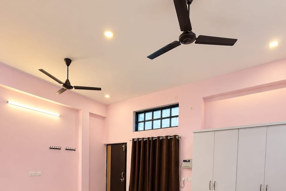 A hotel room with a bed, ceiling fans, a wardrobe, and a window.