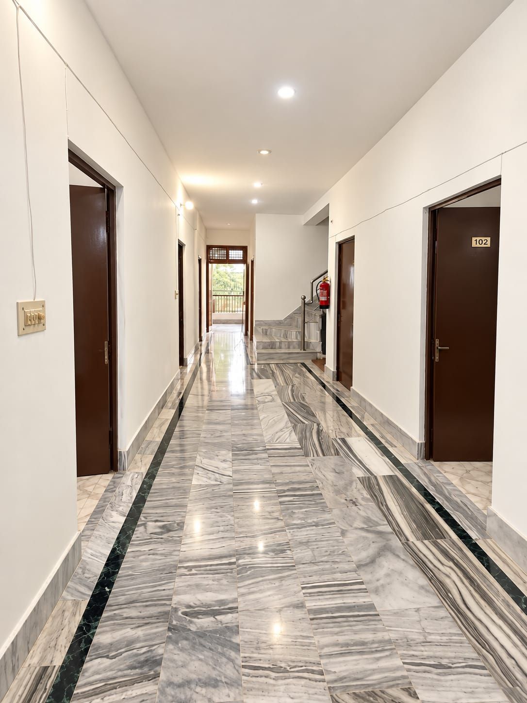A hotel corridor with marble flooring, doors on both sides, and a fire extinguisher mounted on the wall.