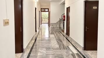 A hotel corridor with marble flooring, doors on both sides, and a fire extinguisher mounted on the wall.