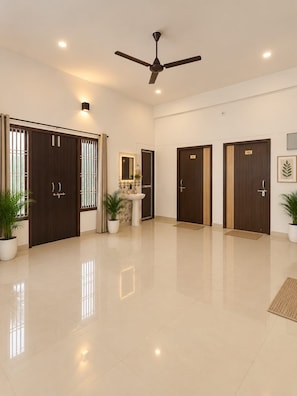 A hotel lobby with a polished floor, a ceiling fan, and a reception area with a counter and a mirror. - Raghav Guest House (Lalpur)