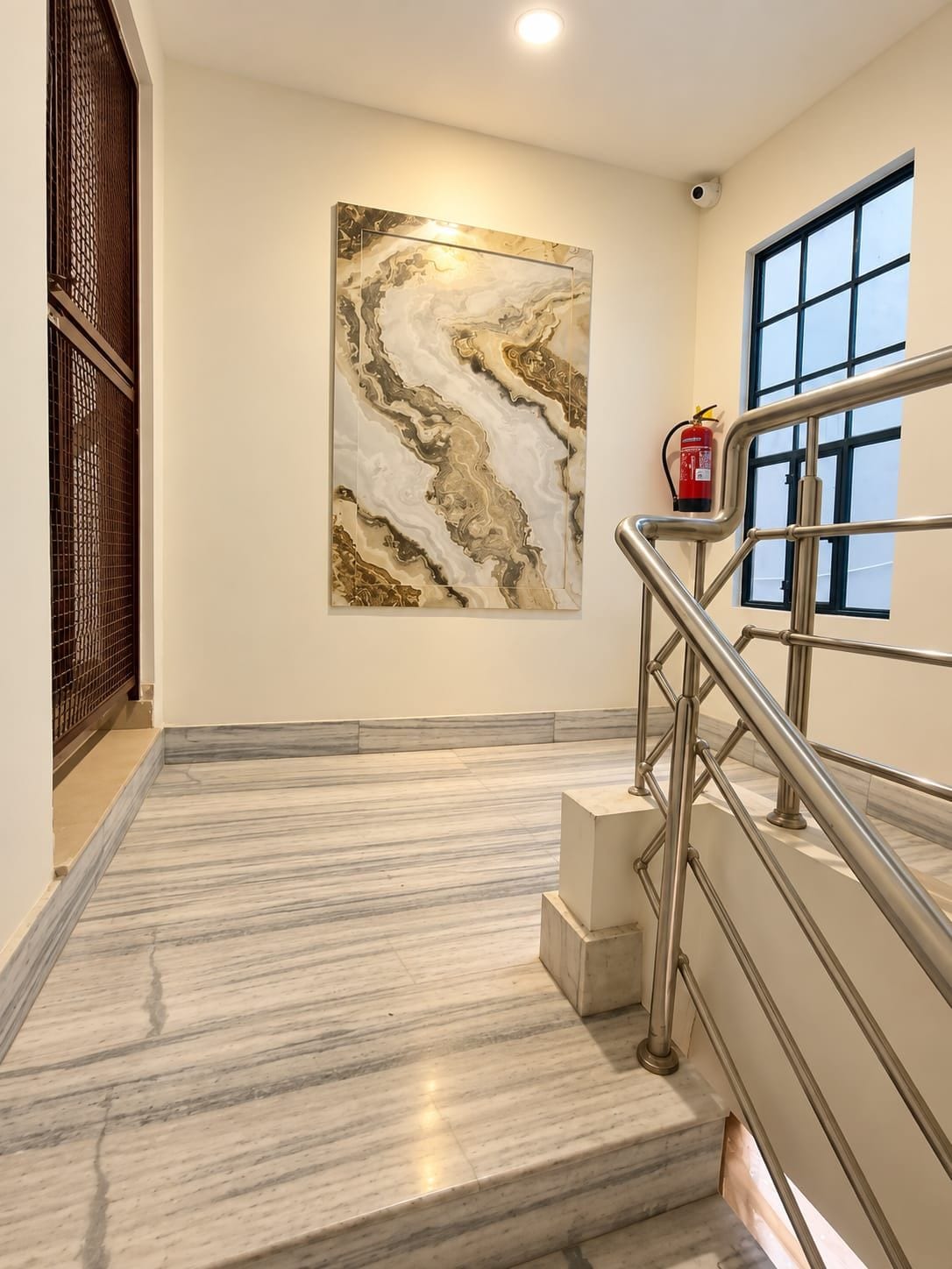 A marble staircase with metal railings and a fire extinguisher mounted on the wall.