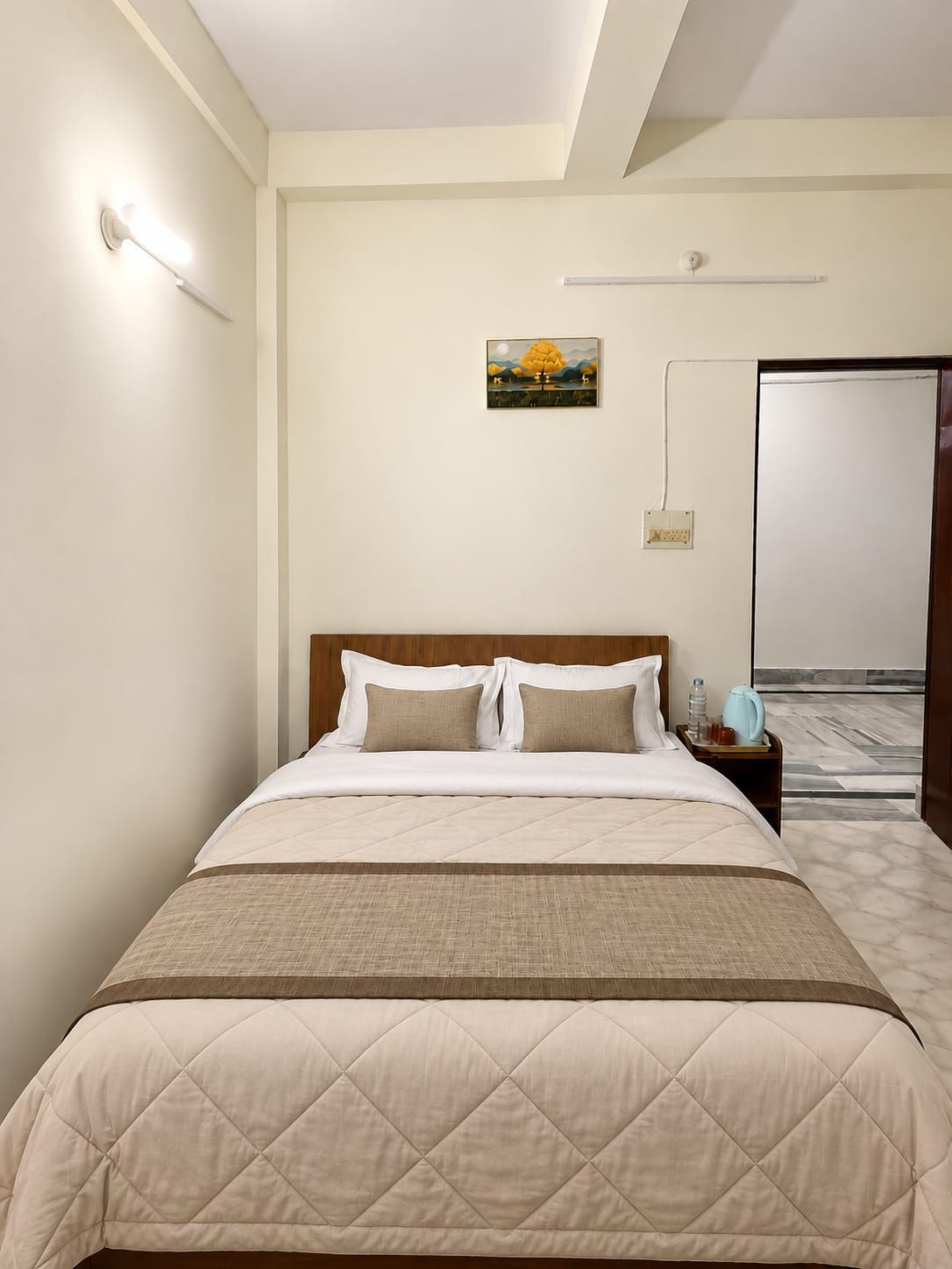 A hotel room with a bed, bedside table, lamp, and a painting on the wall.