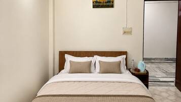 A hotel room with a bed, bedside table, lamp, and a painting on the wall.