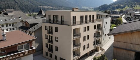 A multi-story building with balconies, situated in a mountainous area with a view of the valley.