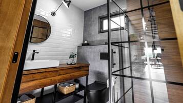 A modern bathroom with a wooden vanity, a round mirror, a white sink, and a glass shower enclosure.