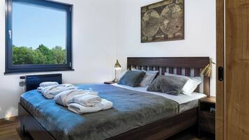 Une chambre avec une grande fenêtre, un lit recouvert d’une couverture bleue, deux lampes de chevet et une carte accrochée au mur.