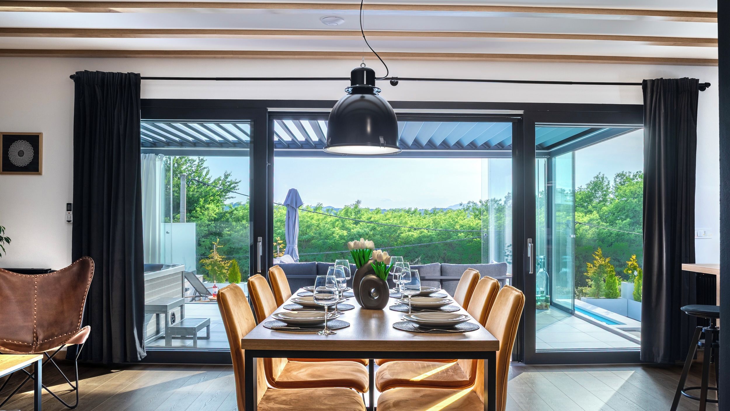 A dining area with a table set for six, large windows, and a view of greenery outside.