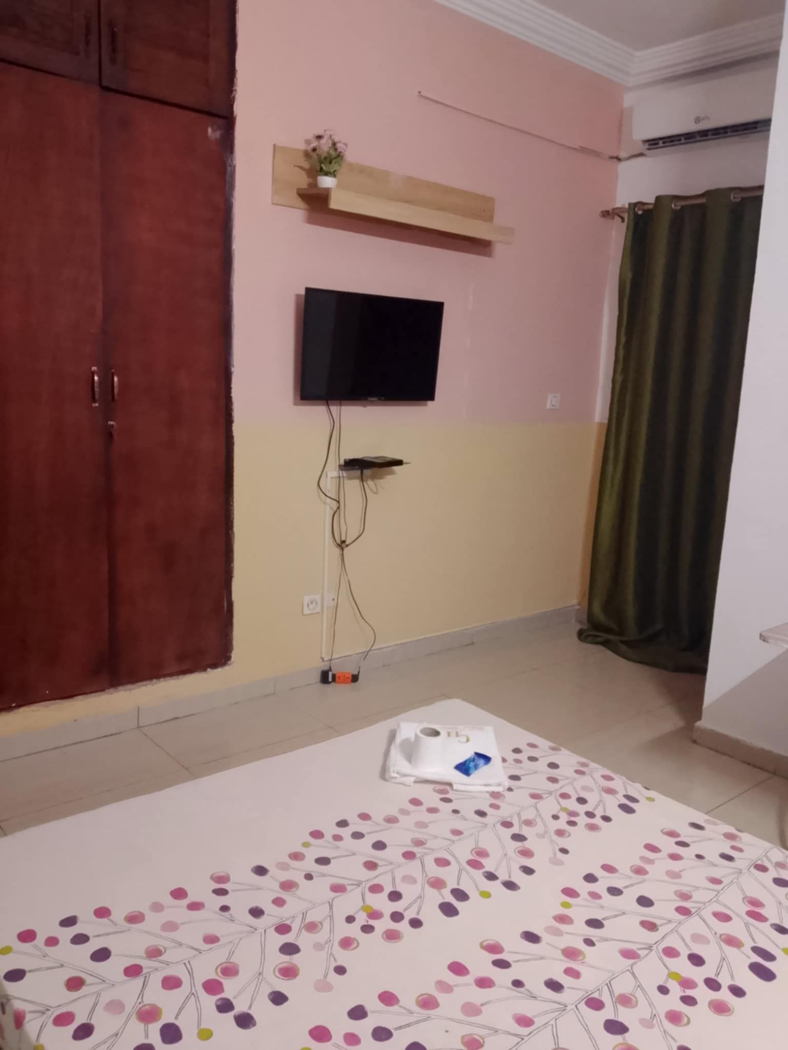 Un dormitorio con cama, televisor montado en la pared, armario y cortina.