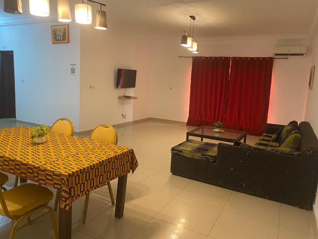 Una sala de estar con un sofá, una mesa de comedor con sillas, un televisor y una cortina roja.