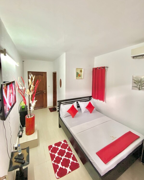 A room with a bed, a TV, a desk, and a door.